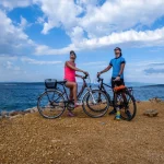 Een stel in sportieve kleding staat op de fiets en bekijkt het weer. Achter hen is de Middellandse Zee. Dikke wolken boven hen. Actieve vakantie. Prachtige kustlijn van Kroatië