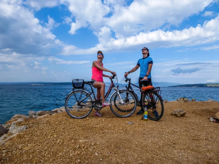 Una coppia in tenuta sportiva, in piedi sulle loro biciclette, controlla il tempo. Alle loro spalle c'è il Mar Mediterraneo. Sopra di loro nuvole dense. Vacanze attive. Bellissima linea costiera della Croazia