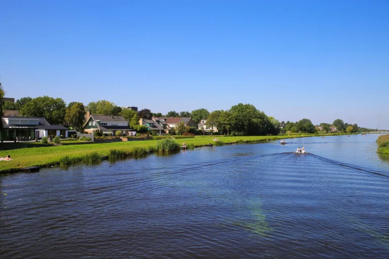 Udsigt over floden Alblas på en eng med beboelseshuse mod blå skyfri sommerhimmel - Alblasserdam, Holland