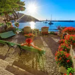 Kvinne i rødt med hatt i Marciana Marina i solnedgangens solstråler, den blomsterrike gamle bydelen Borgo al Cotone: som betyr BOMULLSLANDSBY. Turist på feriereise i Italia. Marciana Marina, øya Elba.