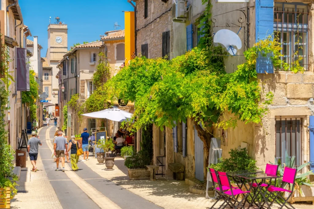 Eine malerische Hauptstraße in der historischen mittelalterlichen Stadt Saint-Remy de Provence, Frankreich, mit bunten Geschäften und Cafés und dem Uhrenturm im Blick an einem Sommertag.