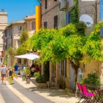 Eine malerische Hauptstraße in der historischen mittelalterlichen Stadt Saint-Remy de Provence, Frankreich, mit bunten Geschäften und Cafés und dem Uhrenturm im Blick an einem Sommertag.